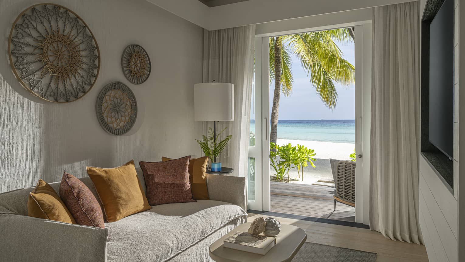 A small room with a sofa, TV, coffee table and walk-out beachfront terrace