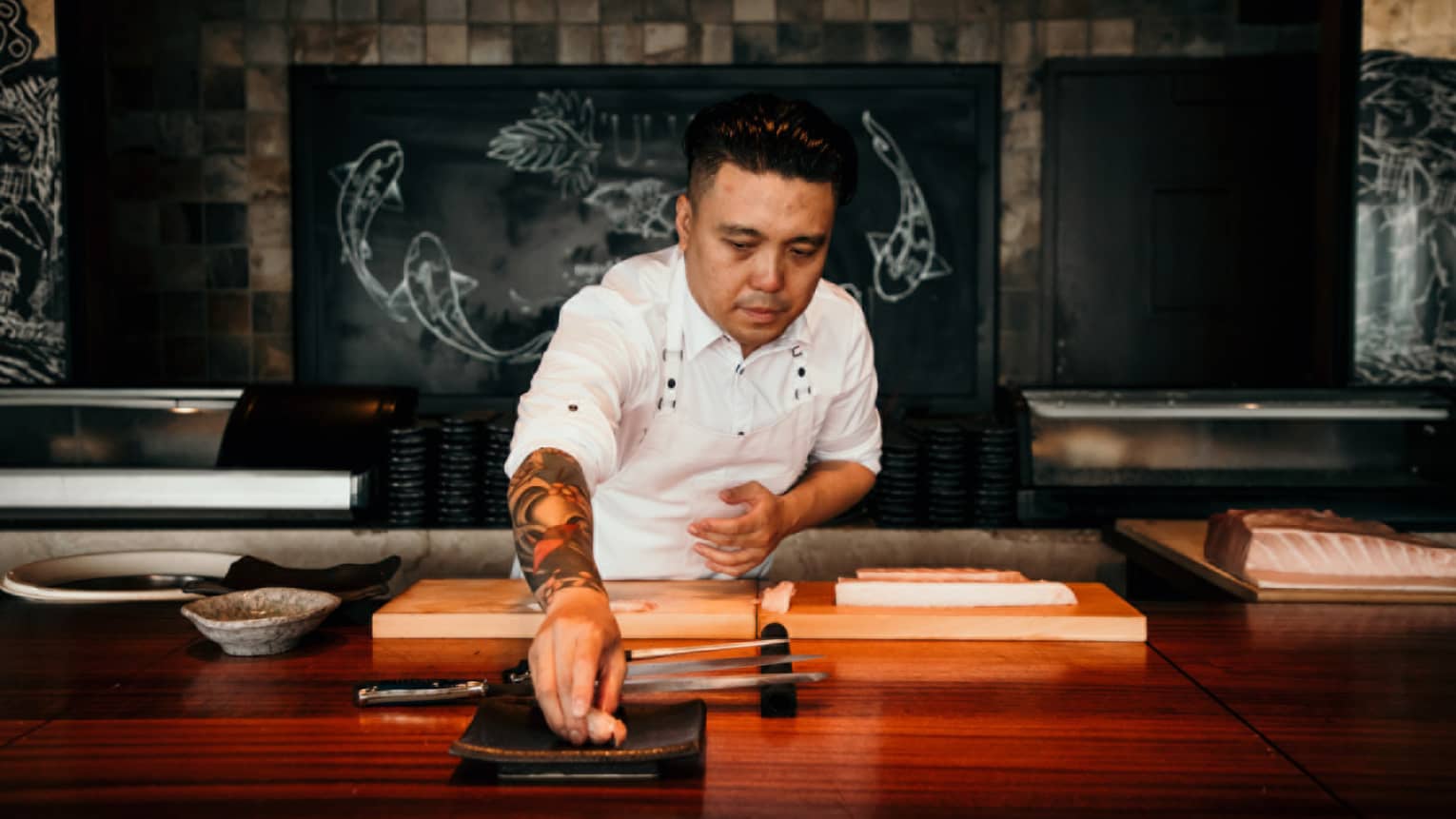 A male chef behind wooden counter places a piece of seafood on plate