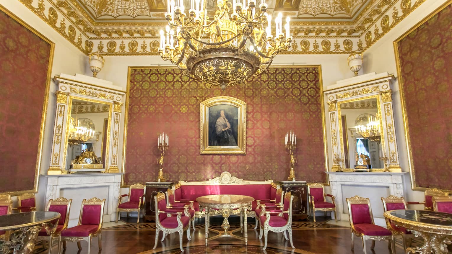Gold ceiling, chandelier over small gold dining tables and chairs with red silk cushions