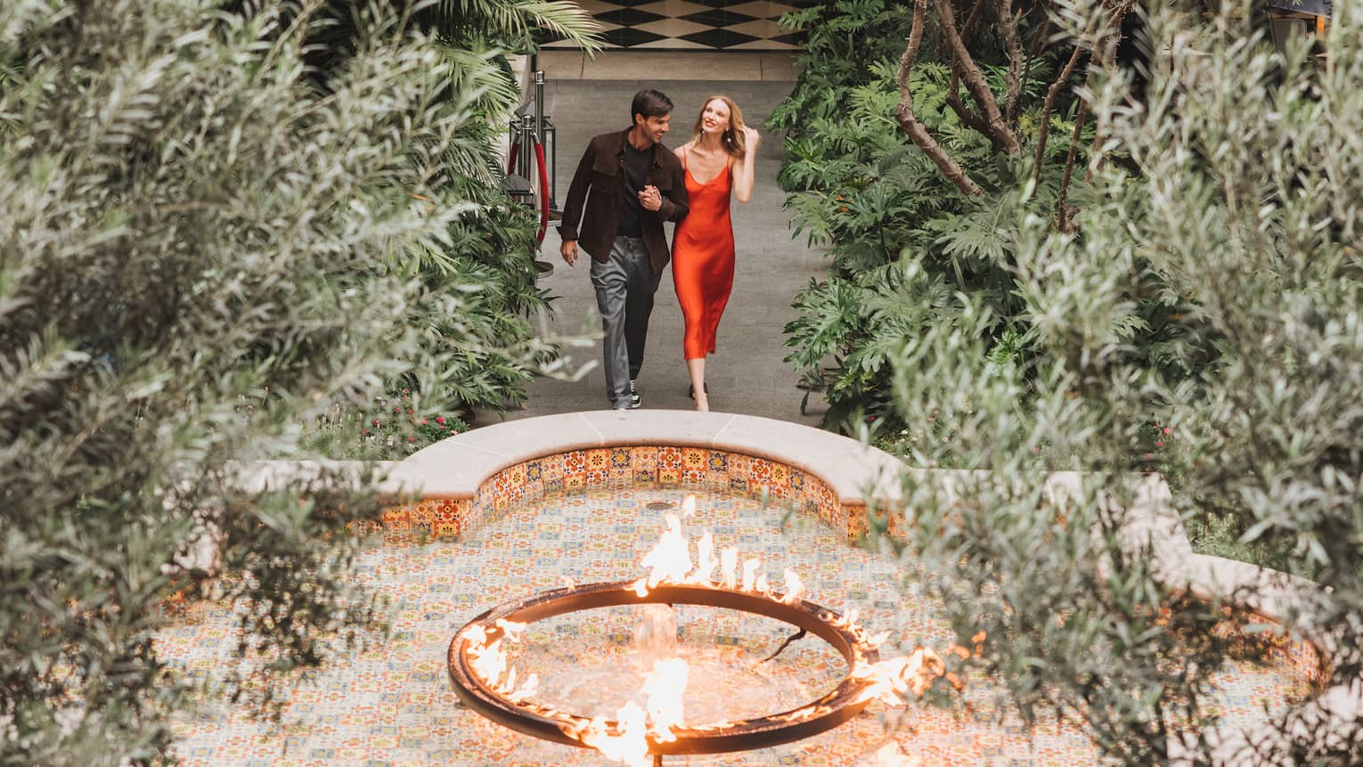 A woman and man walking in a courtyard surrounded by plants and a small fountain.