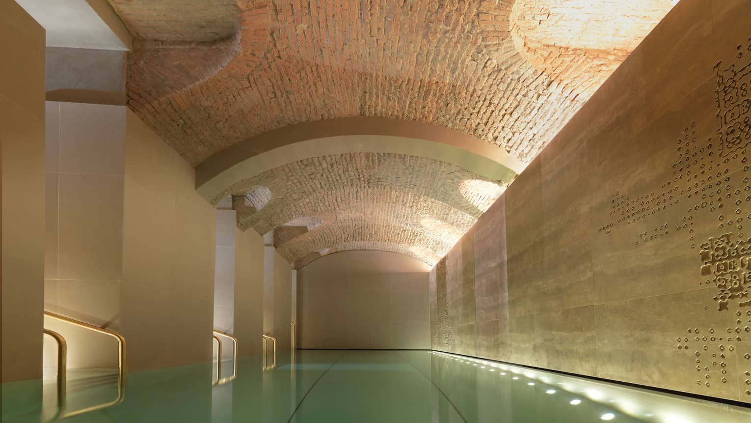 Indoor lap swimming pool with gold railings under curved stone ceiling