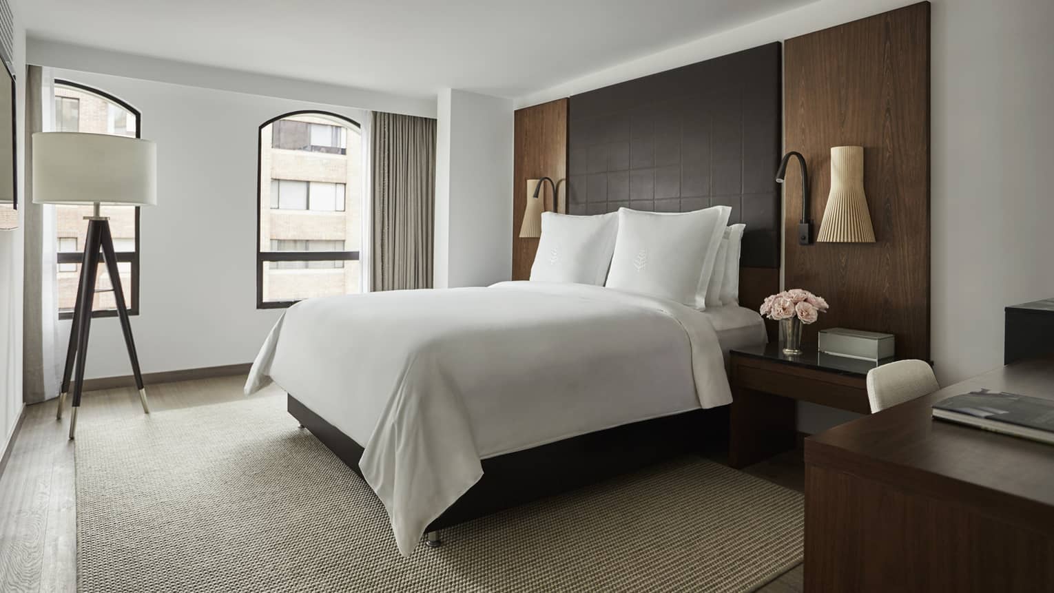Deluxe Room bed with crisp white linens, leather and wood headboard, wood tripod lamp with white shade