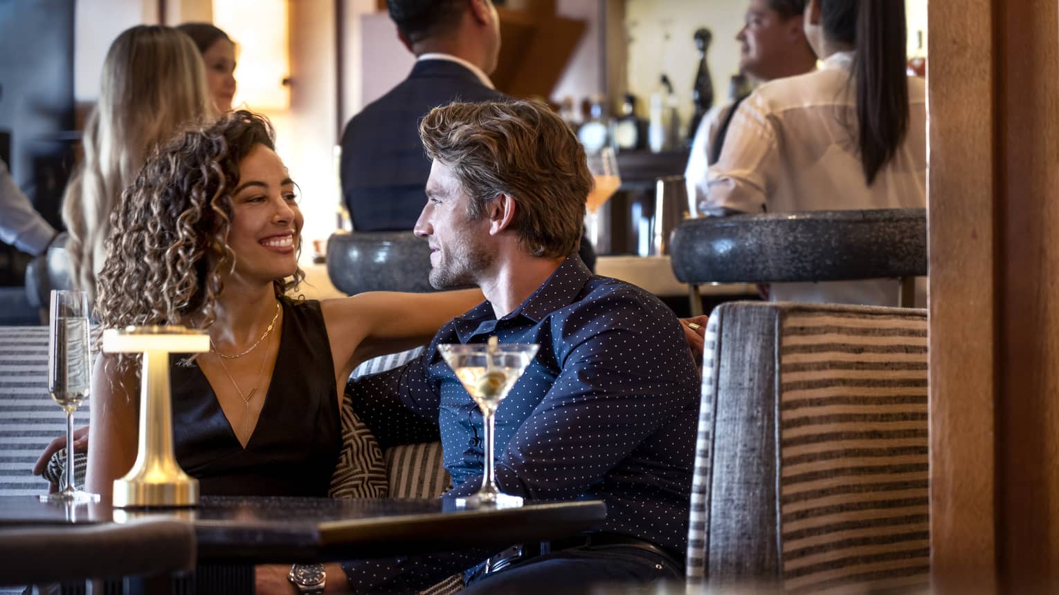 A group of people around a bar and sitting at a table conversing.