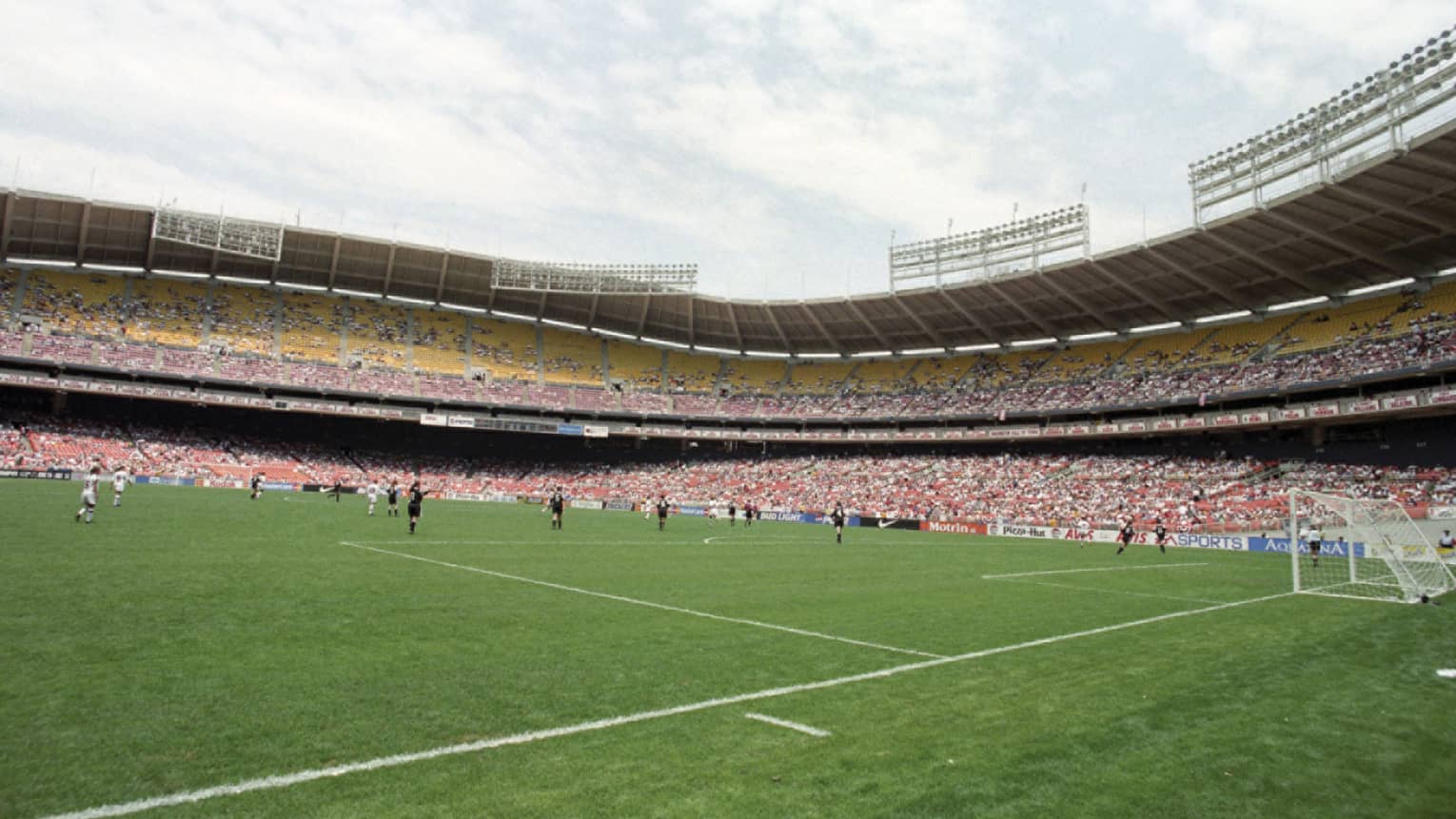 View across soccer field with players below crowds in stadium stands 