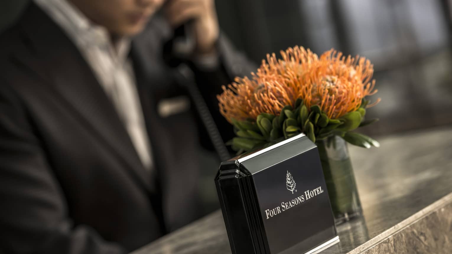 Close-up of Four Seasons Hotel concierge desk, orange flowers in vase, staff on phone