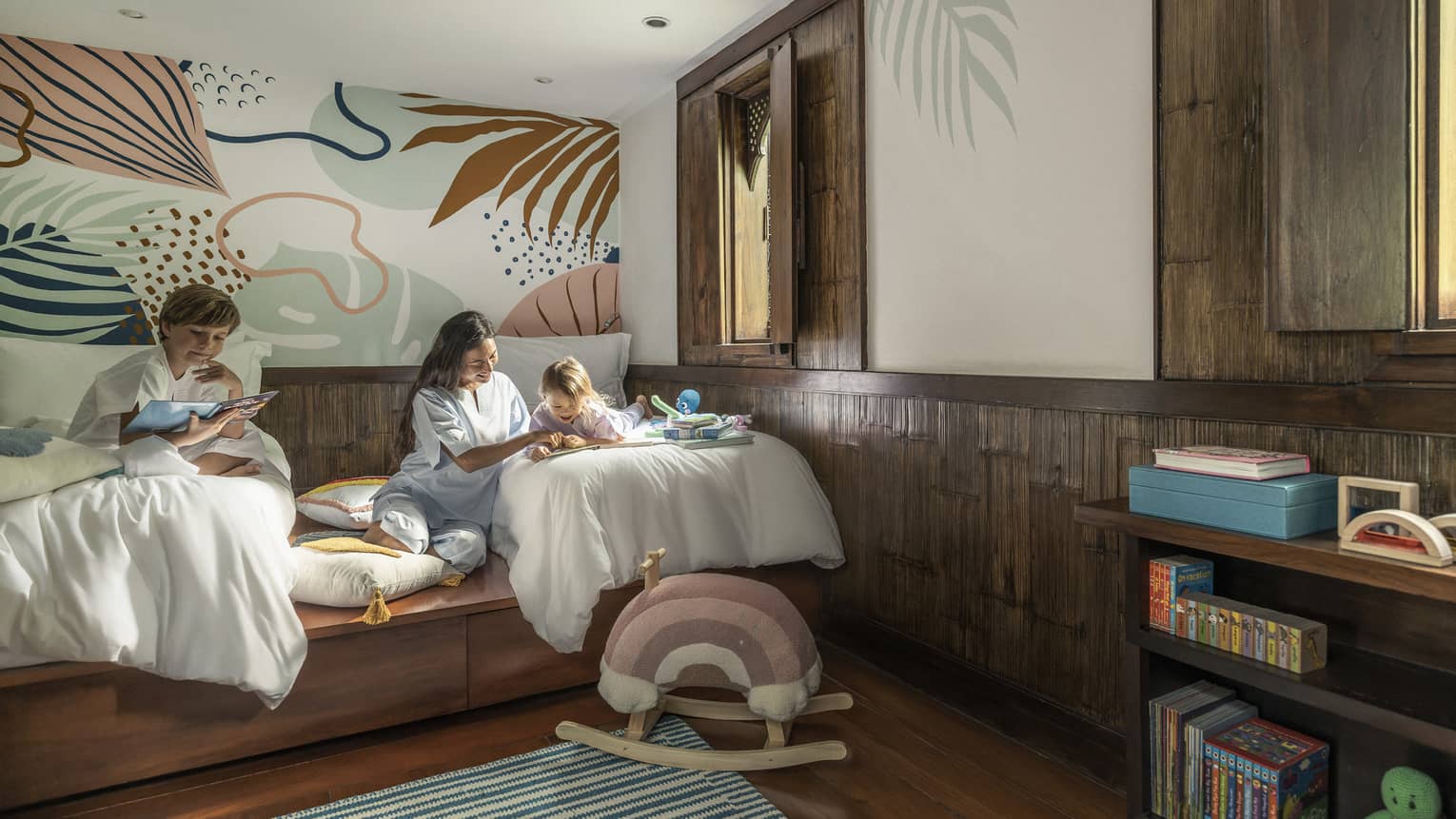 Bedroom with two twin beds, a woman and a man reads to two children