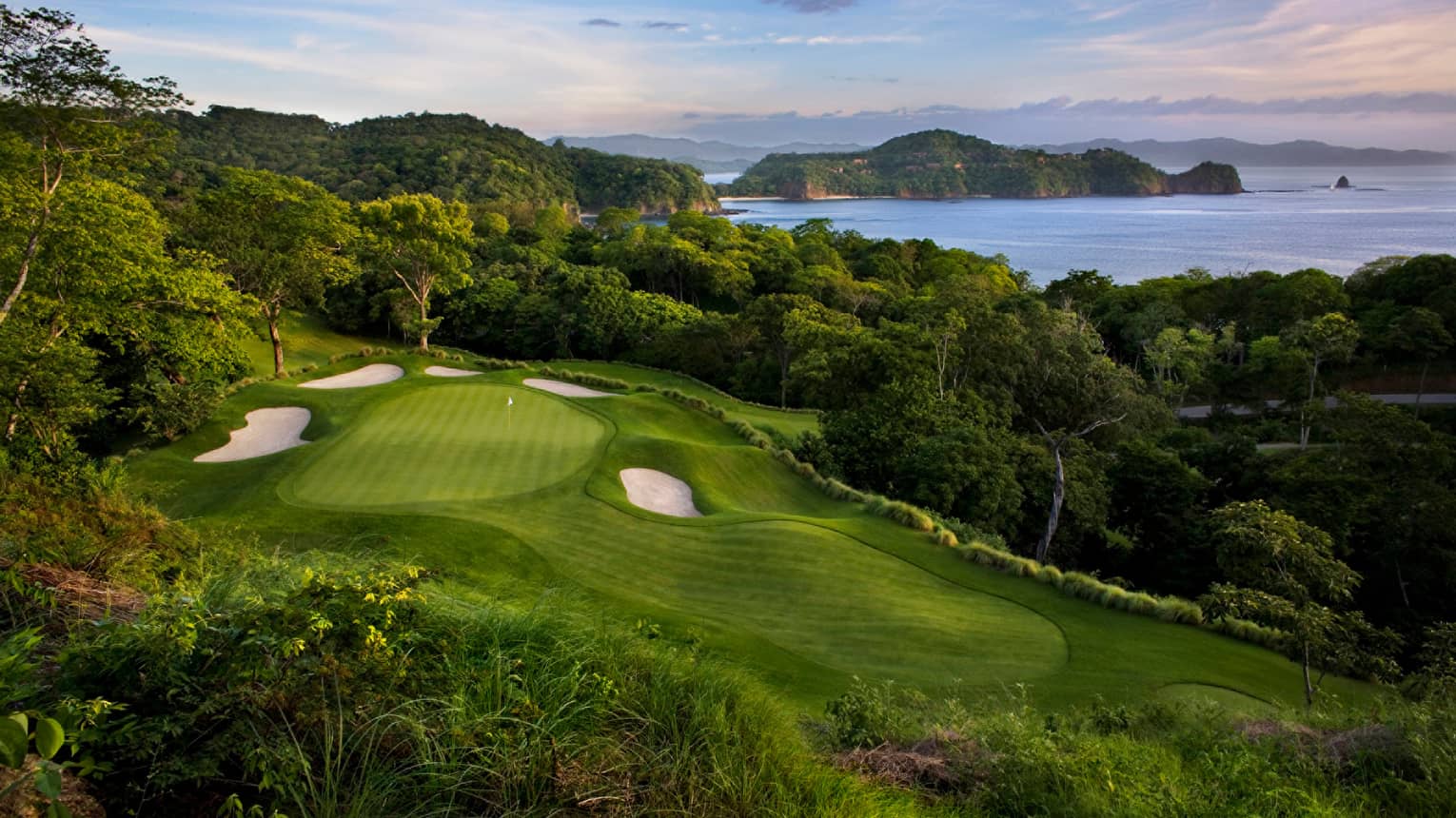 Looking down on golf course green, sand traps on hill overlooking tropical forest, ocean