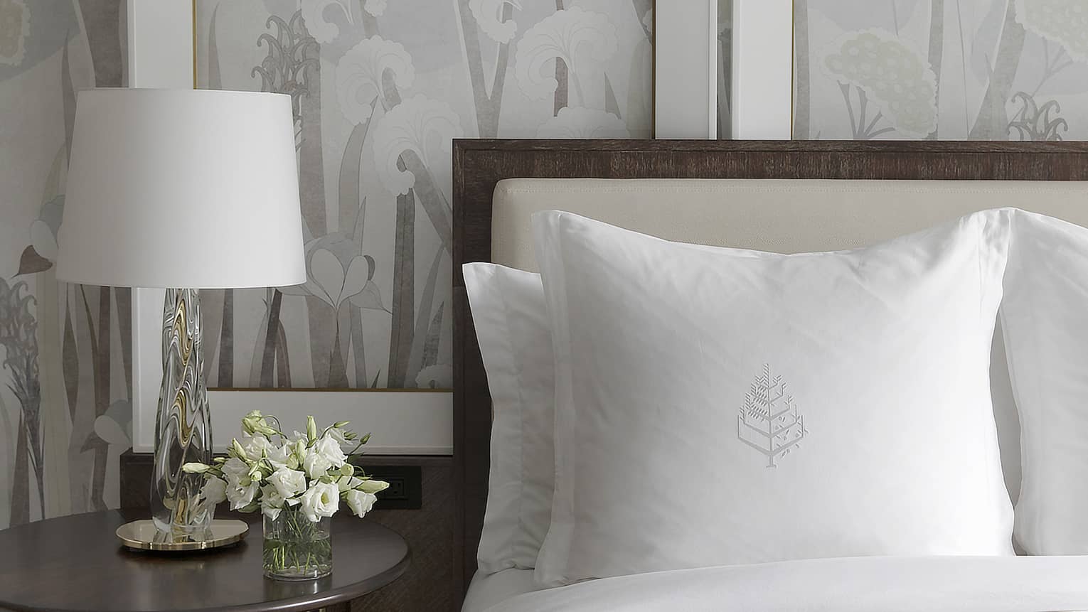 White flowers decorate a bedside table next to a bed with crisp, white sheets
