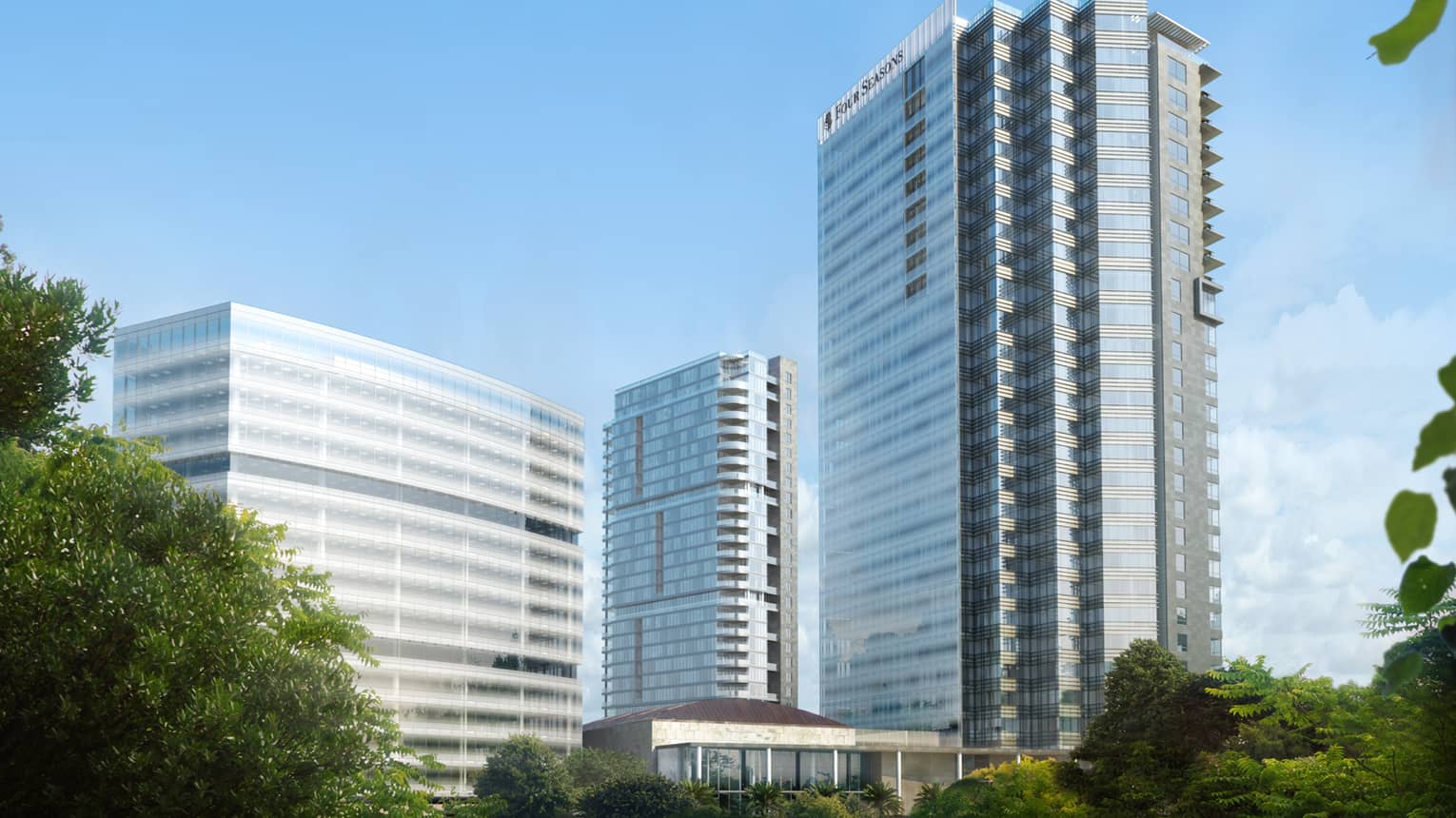 Four Seasons Hotel Bengaluru at Embassy One tall glass towers against blue skies, over canopy of trees