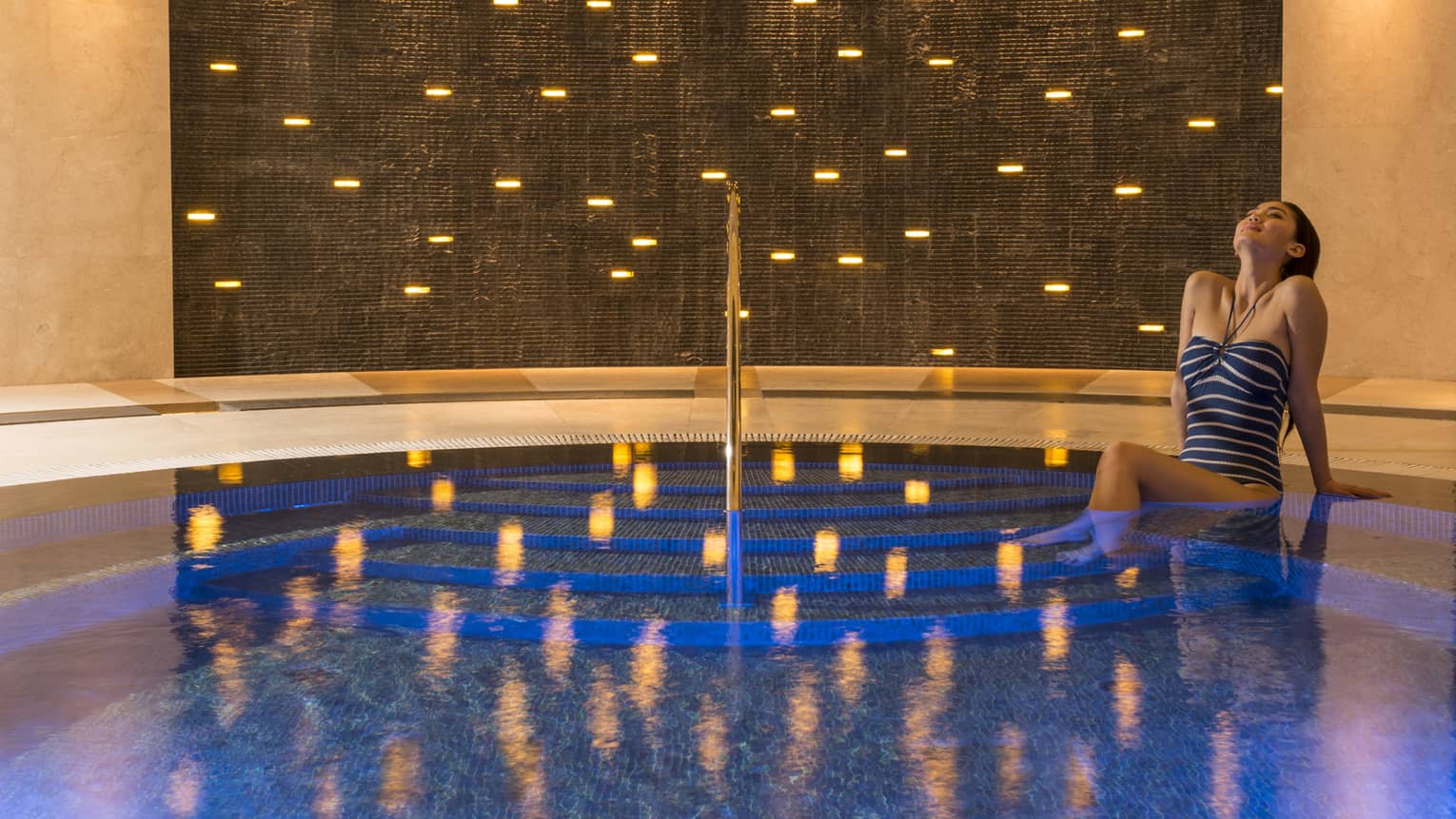 Woman in swimsuit sits on whirlpool steps with lights