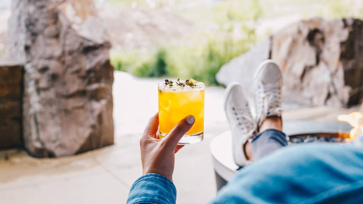 A guest lounges with their feet up, enjoying a cocktail and a view of the mountains