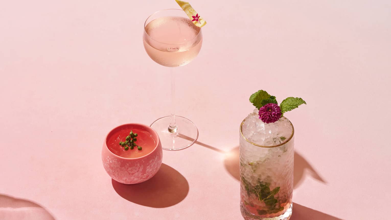 Three cocktails, each in a different type of glass, sit on a pink gradient backdrop