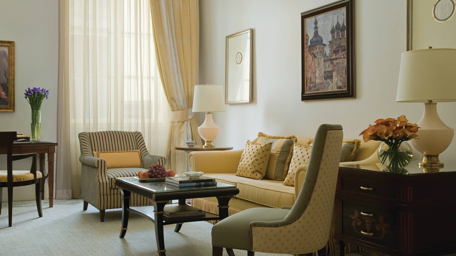 One-bedroom suite seating area with pale yellow sofa, striped armchairs, coffee table, tall window with curtains