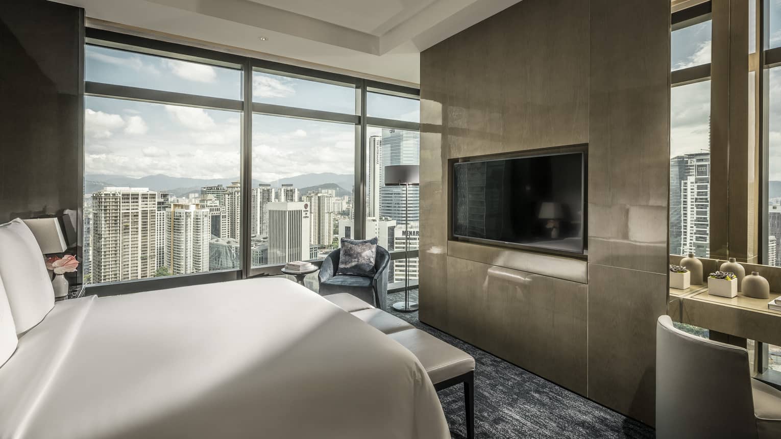Bed across from desk and modern wood panel wall with TV, by floor-to-ceiling window