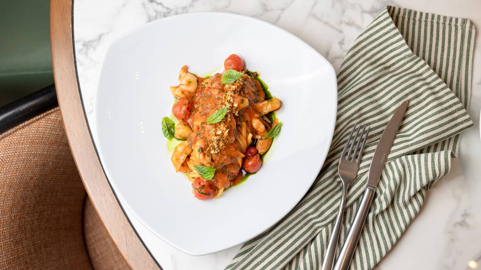 A triangular plate holds a colourful pasta dish with garnishes.