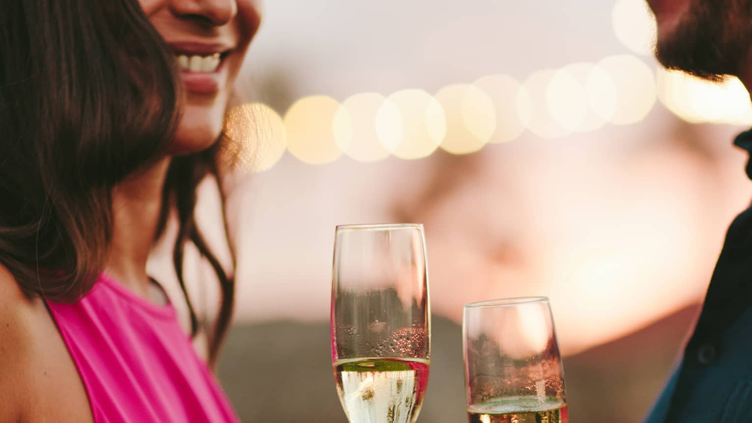 A woman in a fuscia pink dress hold a glass of champagne next to a man with a navy shirt holding his own glass 