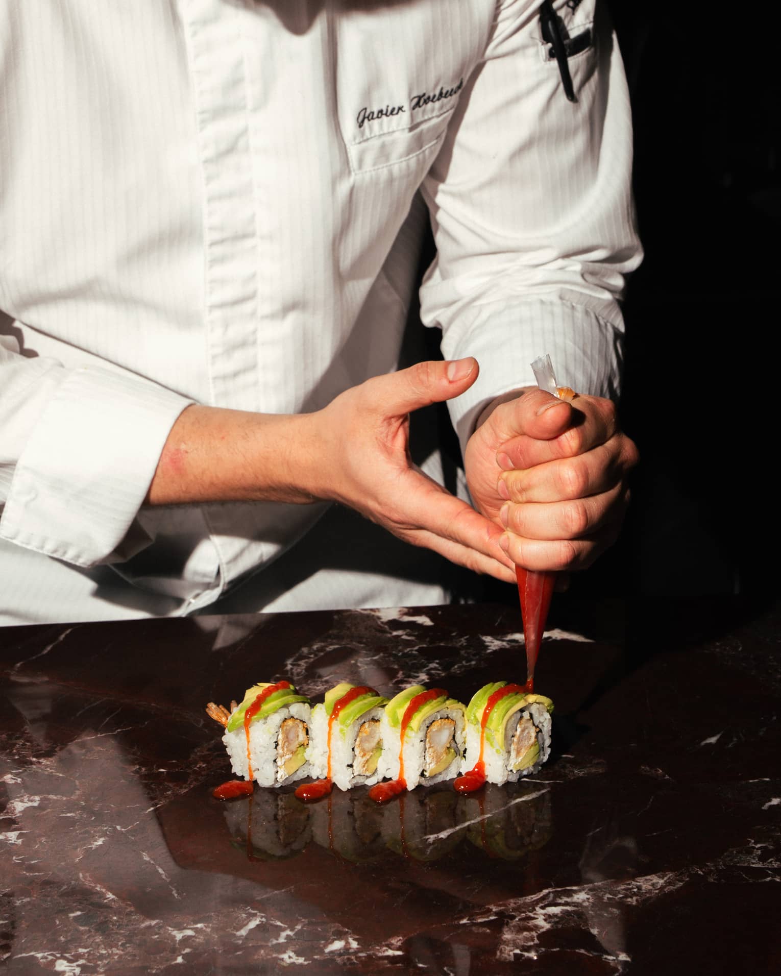 A chef adds garnish to a row of sushi rolls.