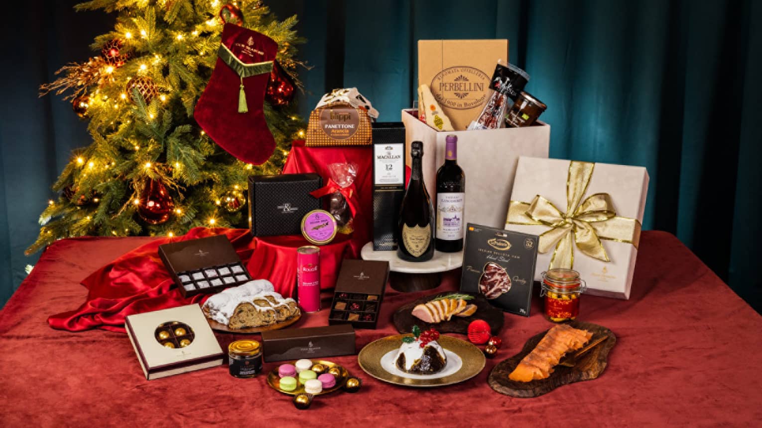 Festive hamper display on table with red tablecloth, Christmas tree in background