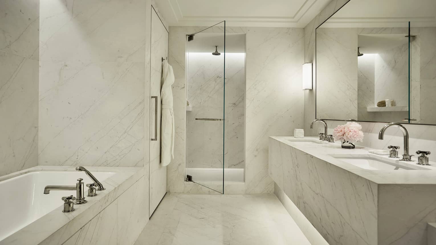 Luxury hotel bathroom with a marble bathtub, double sink vanity, walk-in shower with a glass door and elegant lighting
