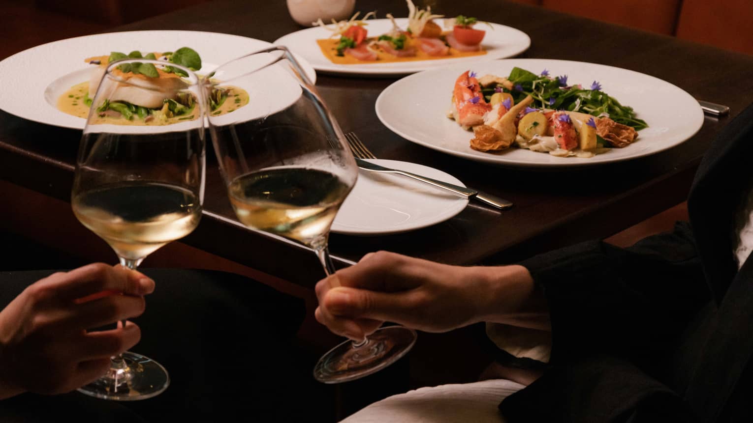 Two people clink glasses of white wine at restaurant table