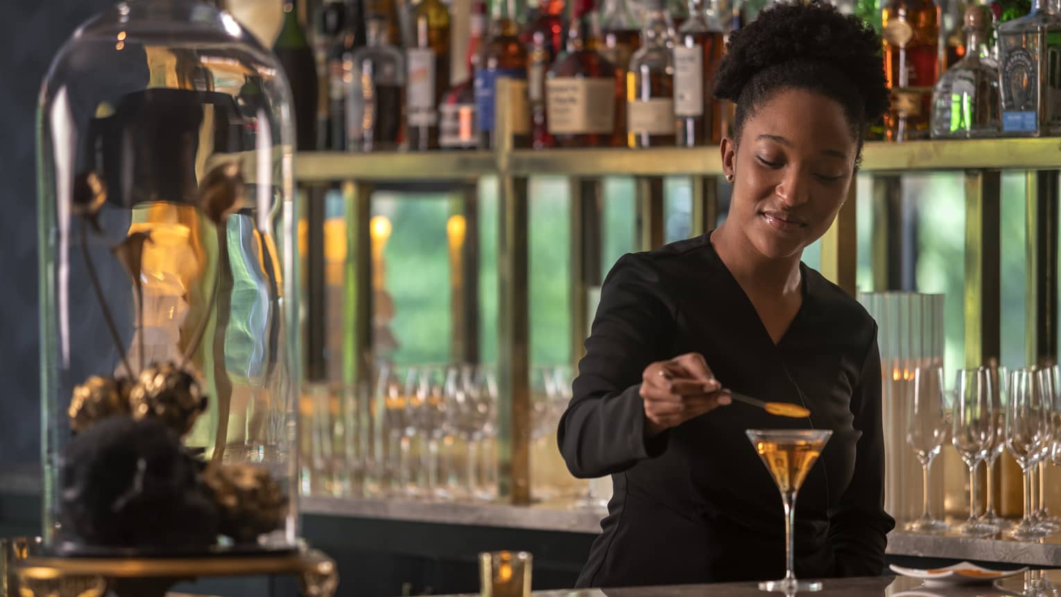 Bartender places the finishing touches on a cocktail, rows of liquor bottles on display behind her