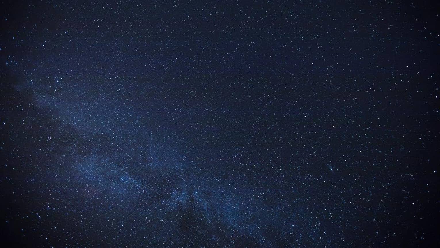 Thousands of stars dusting across a clear night sky; a cluster of stars form the Milky Way, just barely visible in the sky.