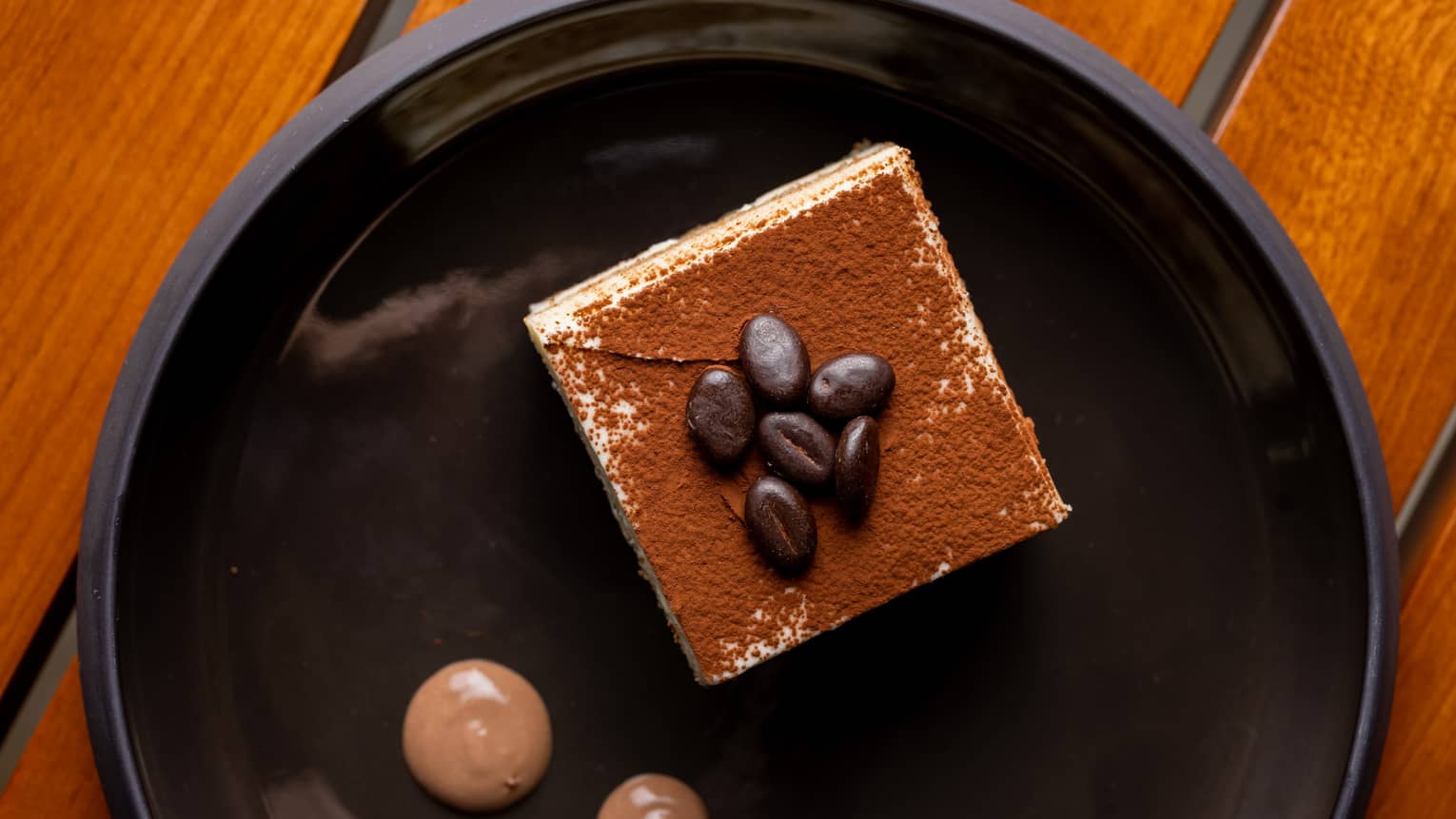 A slice of tiramisu on a black plate.