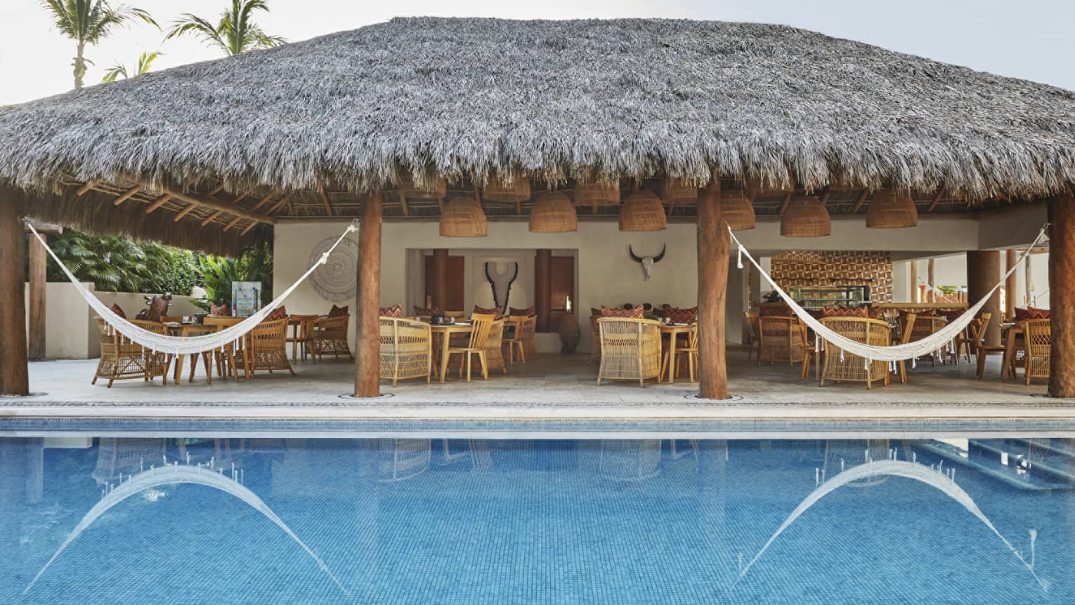 Outdoor lounge set under thatched-roof pavilion next to pool