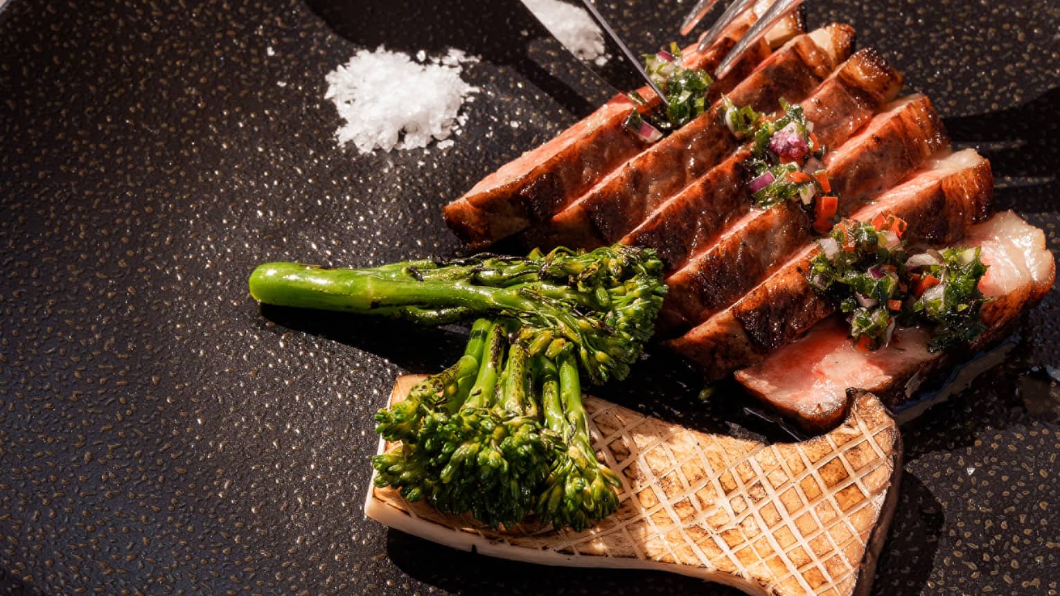 A cut of Wagyu beef tossed with salt and steamed broccoli on a black plate.