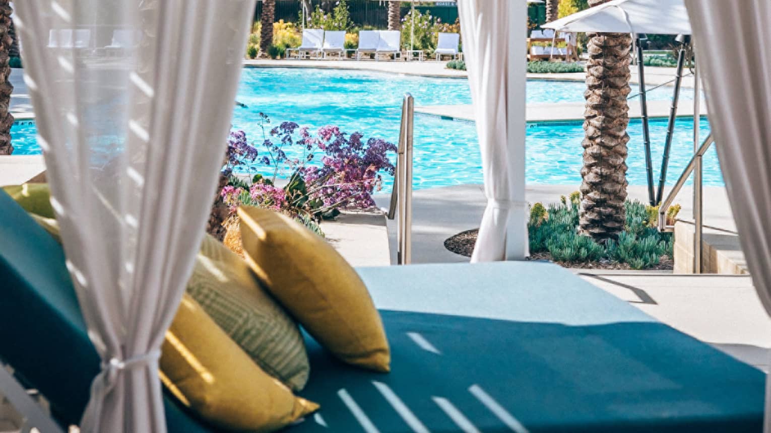 Poolside cabana featuring a blue daybed with yellow pillows and sheer beige curtains
