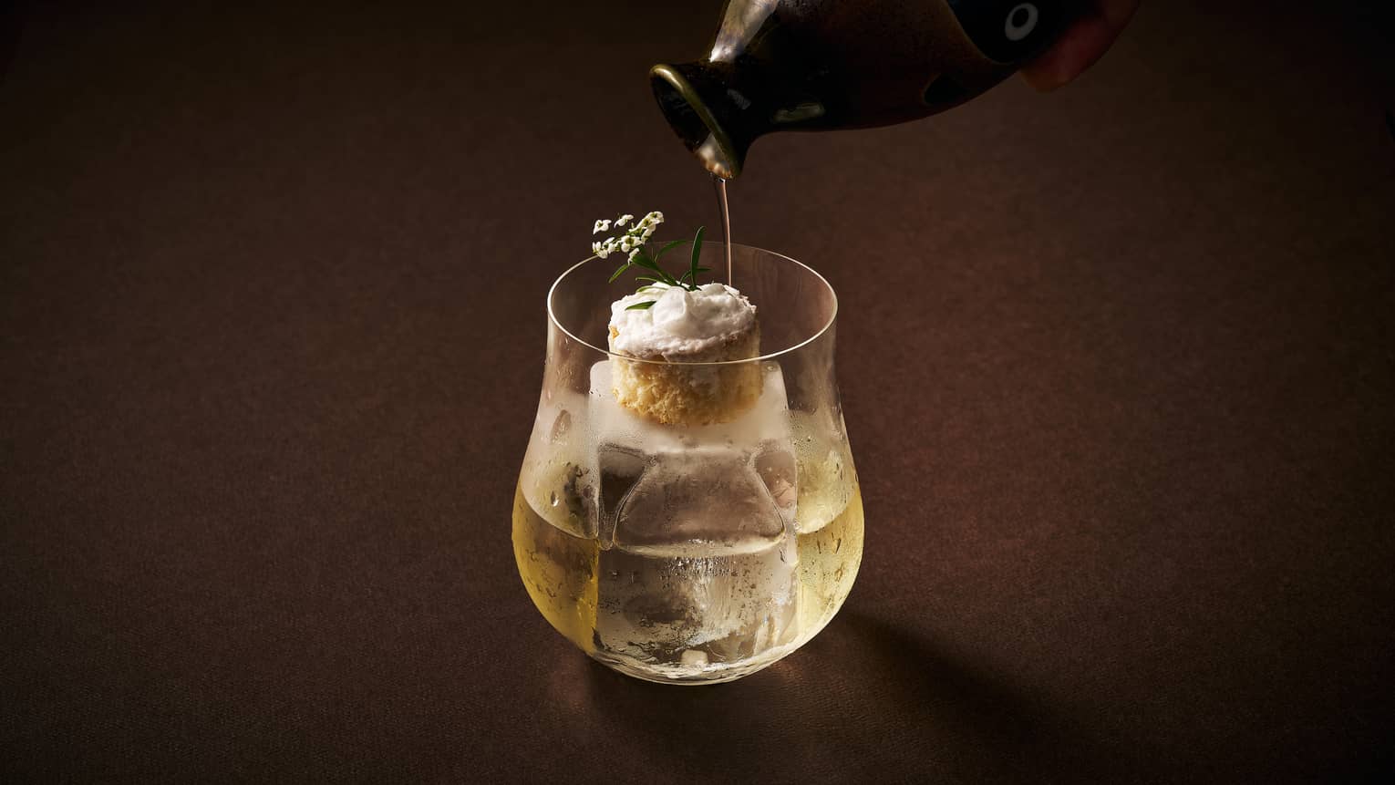 Cocktail topped with a miniture dessert atop a square ice cube