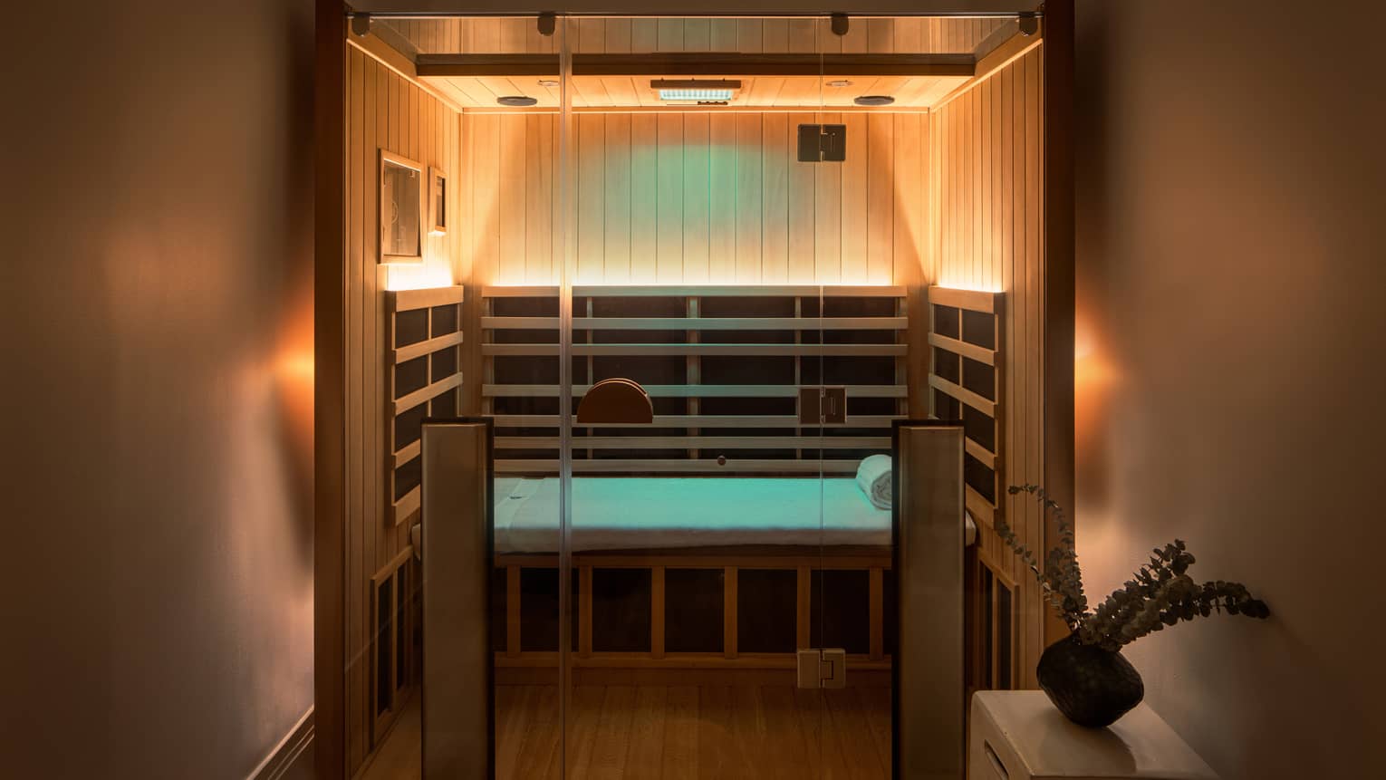 Wooden infrared sauna with lowlighting, side table with vase of eucalyptus 
