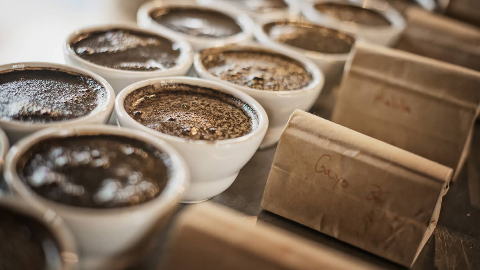 Dark coffee in white porcelain ramekins next to kraft paper bags.
