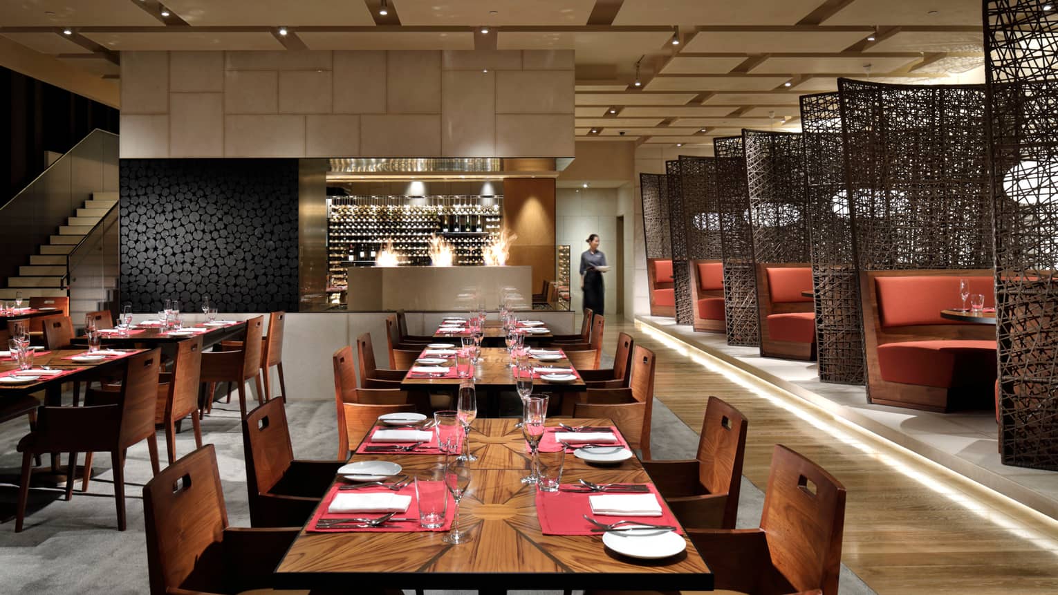 Modern dining room with rows of wood tables, large wine cellar, booths by black woven screens