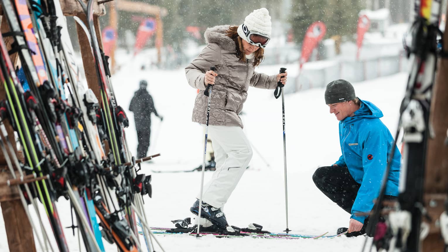 Ski concierge kneels down by woman trying on skis in front of rack