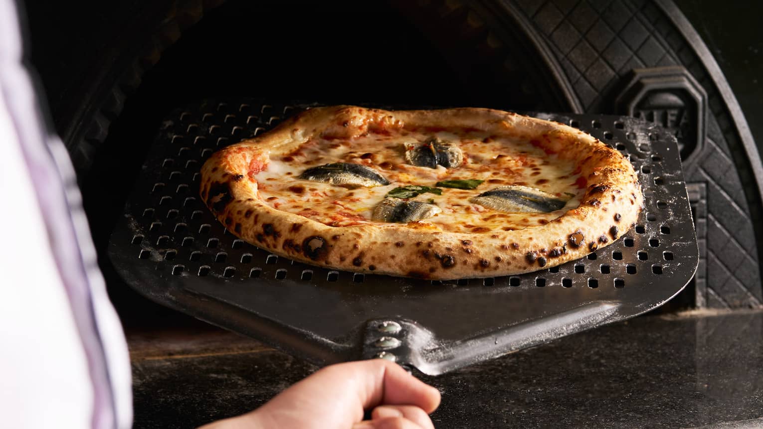 Chef removes golden brown pizza from oven on pizza peel