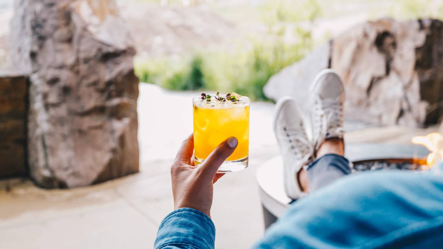 A guest lounges with their feet up, enjoying a cocktail and a view of the mountains 