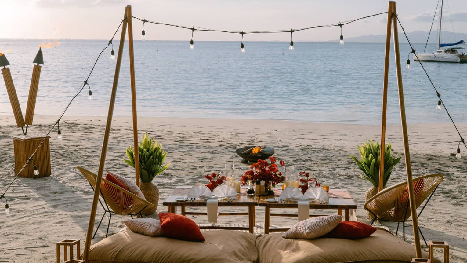 Private dining set up on a beach with two cusions, a table, string lights and rustic decorations