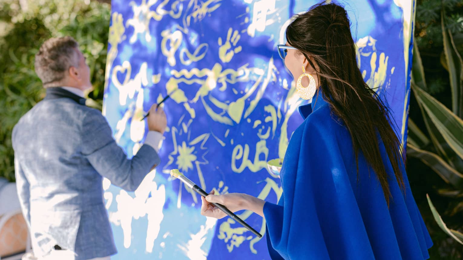 A man and woman painting on a large canvas.