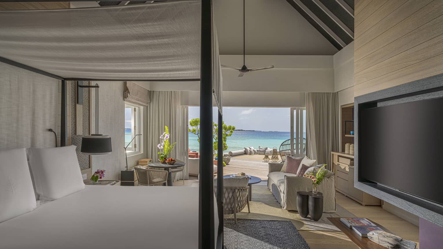 Luxury bedroom with four-poster bed, sitting area and walk-out terrace facing tropical beach