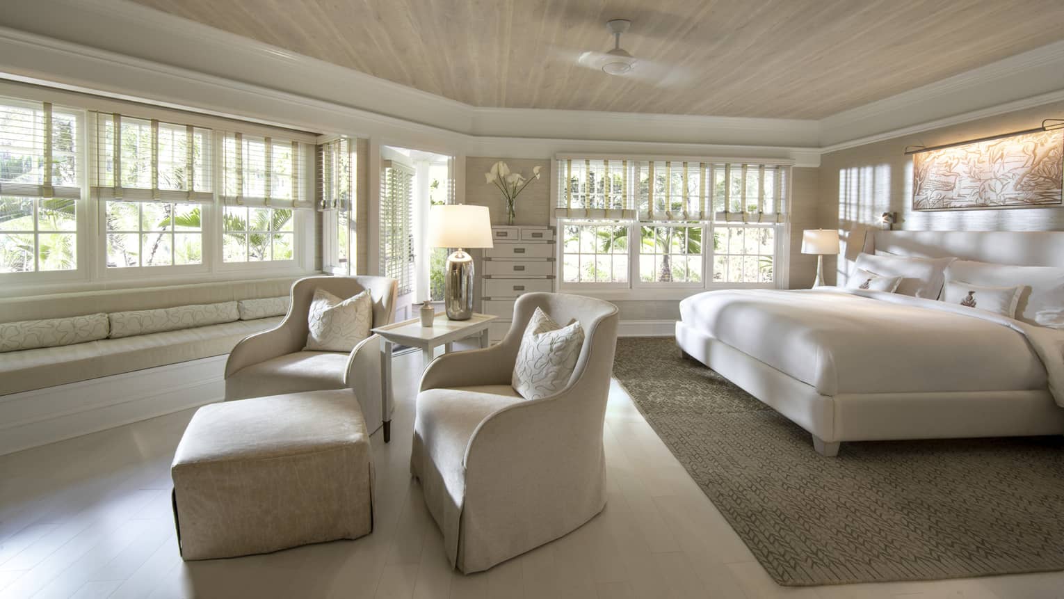 Deluxe bedroom with all-neutral king bed, two club chairs and ottoman facing expansive windows