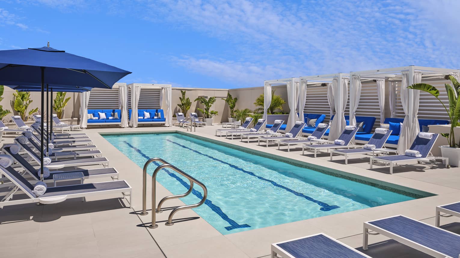 Rectangular pool with blue lounge chairs and umbrellas.
