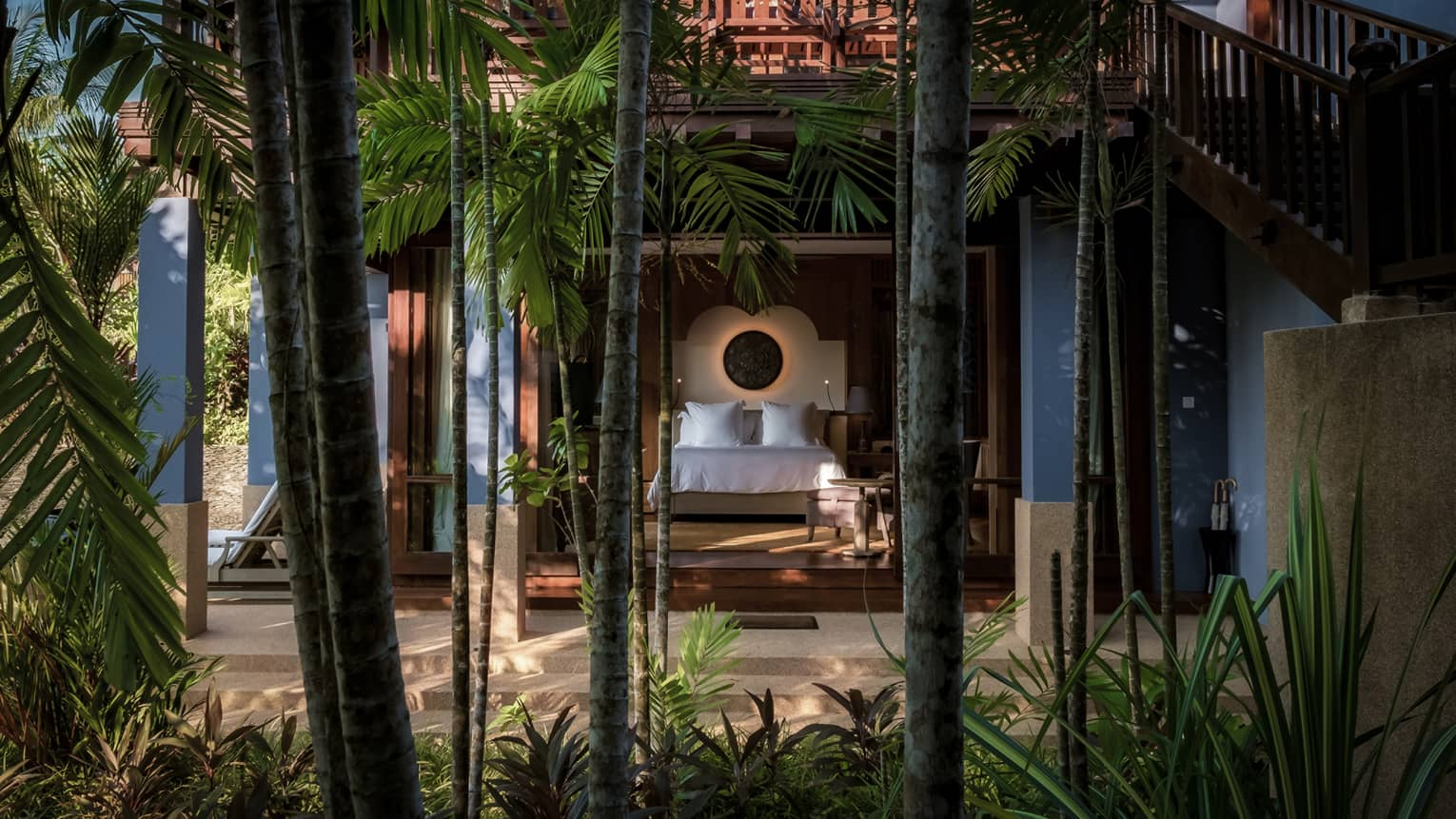 Garden View Pavilion bedroom from behind tall palm tree trunks