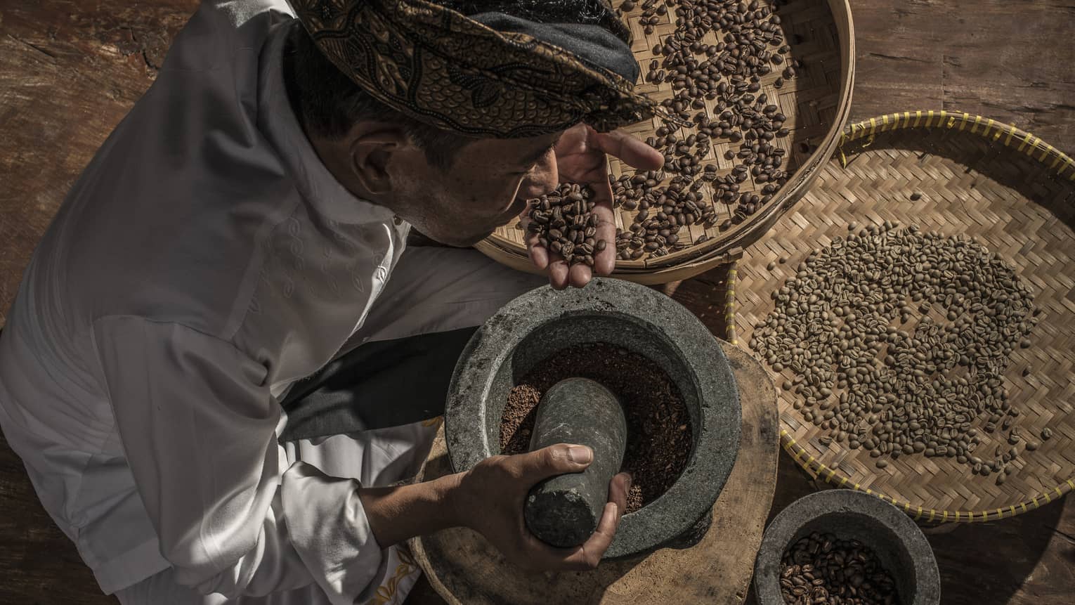 A coffee grower with coffee beans in a large mortar and pestle at Four Seasons Bali and Jimbaran Bay