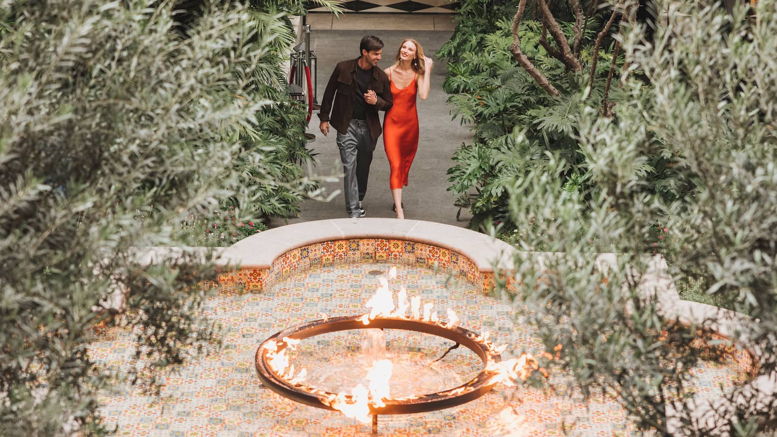 A woman and man walking in a courtyard surrounded by plants and a small fountain.
