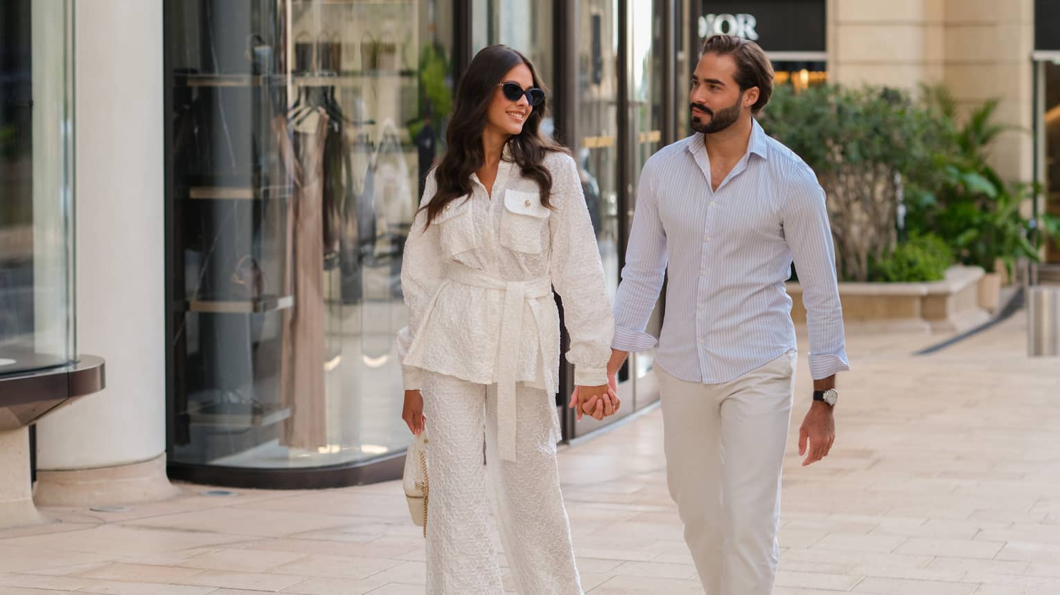 A couple holding hands while walking down a city street filled with shops