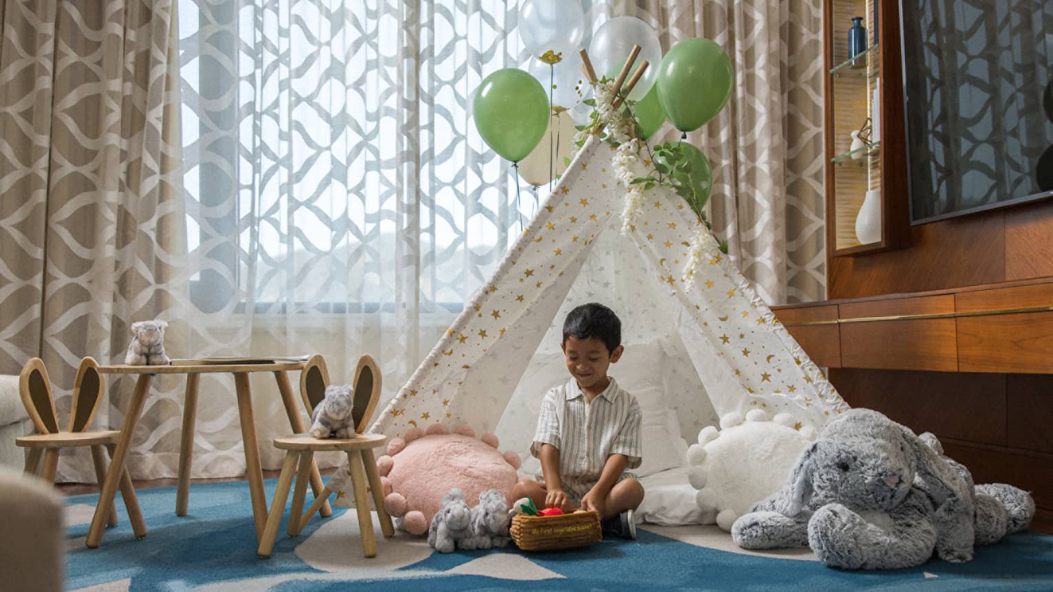 Boy sits on carpet in kid tent with balloons tied to it