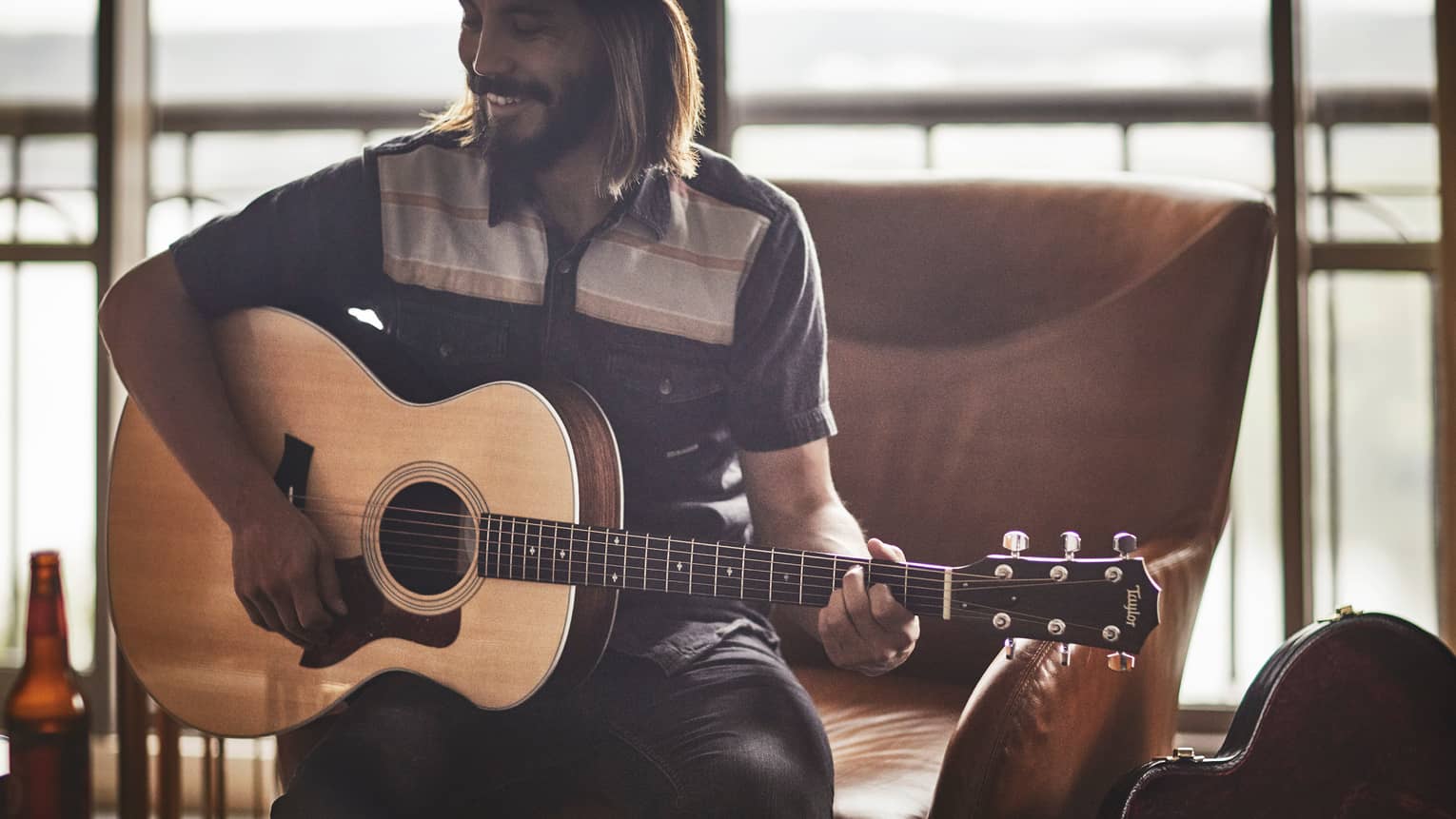 Smiling Guitar Concierge with long hair, beard, hat plays acoustic Taylor guitar