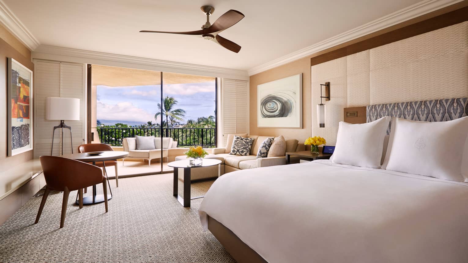 Spacious resort room with king-sized bed, seating area, balcony with tropical view, ceiling fan and modern decor