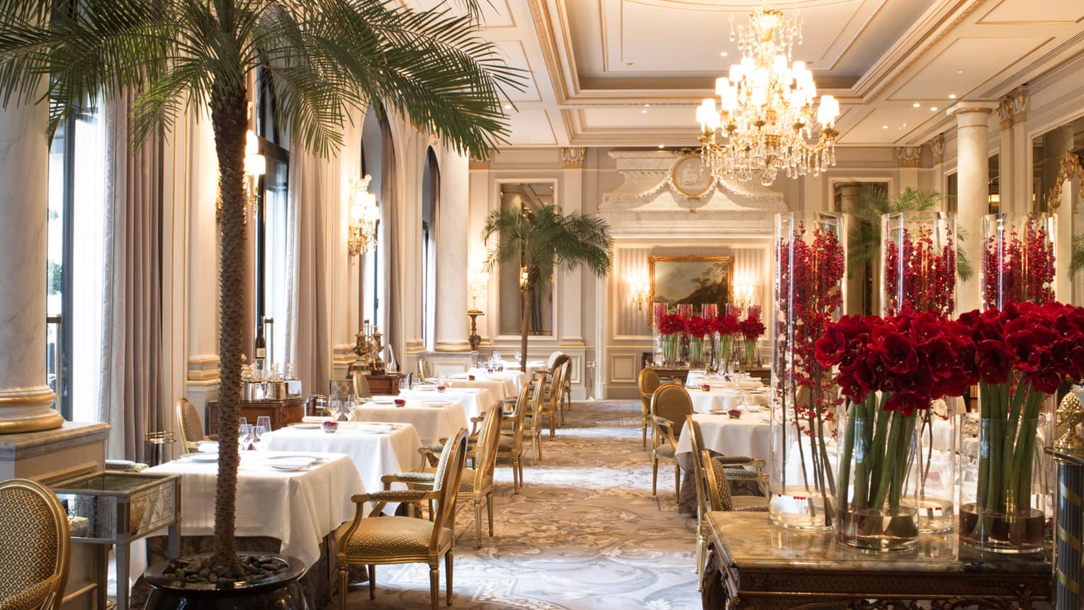 Potted palm trees, red flowers, crystal chandeliers decorate elegant dining room